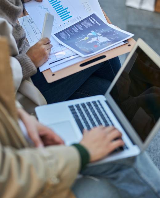 Close up of businesswoman holding cellphone and studying documents while her colleague using laptop on the street